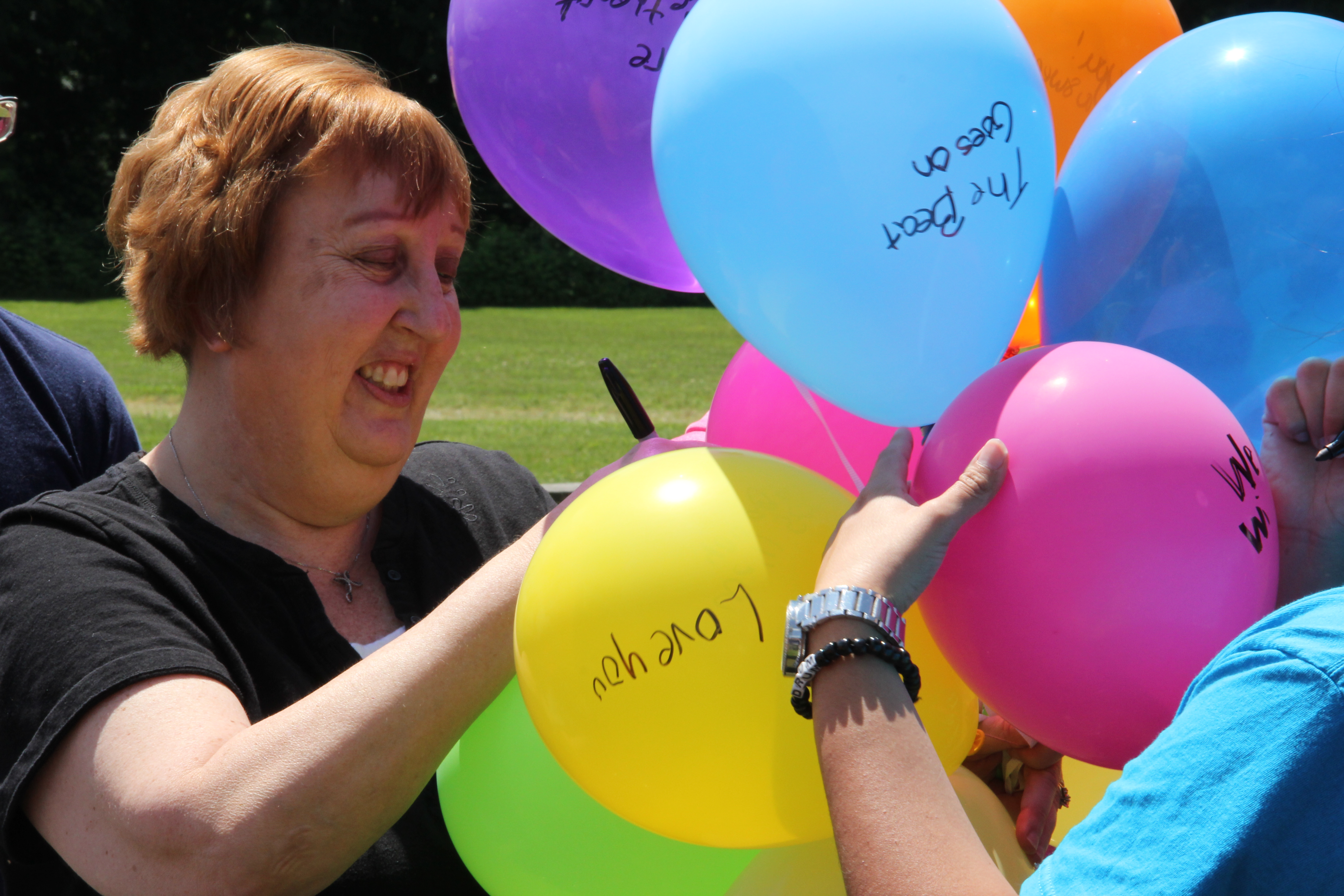 Anne Cripe writes messages on balloons during a memorial service for Mark Cox at ADEC Monday.